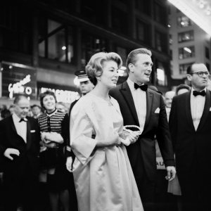 La imagen muestra al actor Kirk Douglas y a su mujer vestidos de gala, cruzando una calle. La imagen está tomada desde muy cerca, como si Vivian estuviera en medio del gentío que esperaba a los actores, que pasan delante de ella sin mirar. Pulse para ampliar.